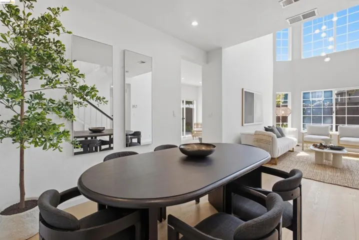 Open-concept living space with light wood-finish flooring, high ceilings, and abundant natural light from tall windows
