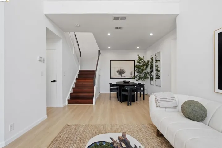 Open-concept living area featuring light wood-finish flooring, recessed lighting, and a contemporary staircase with dark wood treads and a white railing