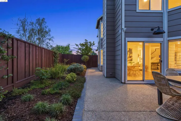 Exterior featuring gray horizontal siding, an exposed aggregate patio, and a dedicated garden bed with mature plantings