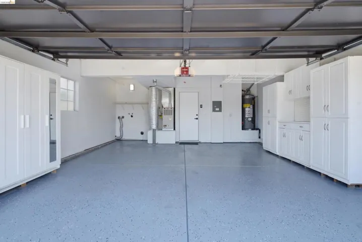 Spacious garage featuring an epoxy-coated floor, extensive built-in white cabinetry, a built-in water heater, and a horizontal window providing natural light