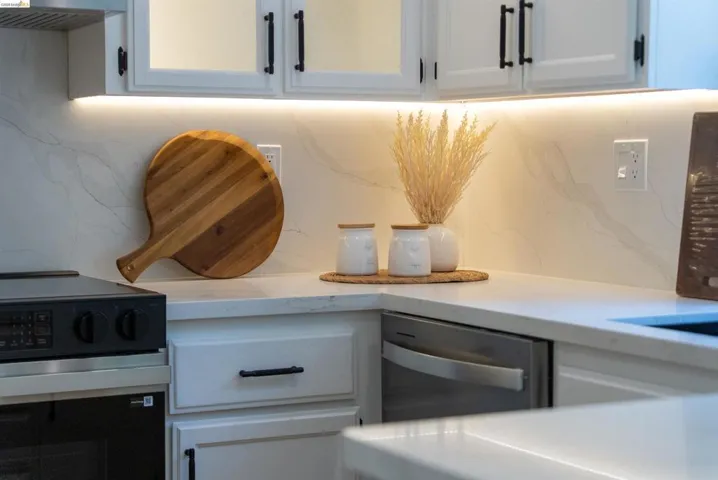 Modern kitchen featuring white cabinetry with black hardware, under-cabinet lighting, and a white countertop with a matching backsplash