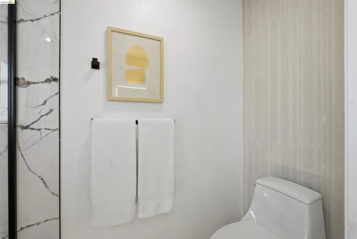 Modern bathroom featuring a walk-in shower with black-framed glass enclosure, large-format marble-look wall tiling, and a built-in toilet