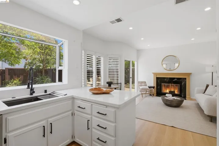 Contemporary kitchen and living area featuring white cabinetry with matte black hardware, light-toned wood-finish flooring, and recessed lighting