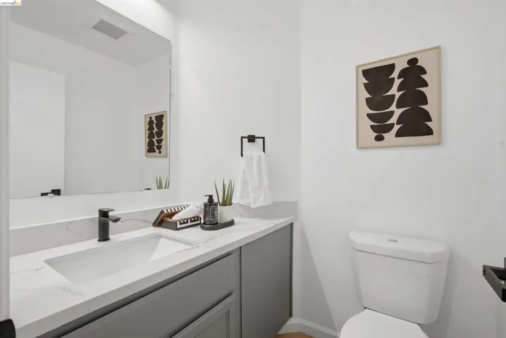 Powder room featuring a sleek white toilet, grey vanity with a white countertop, rectangular undermount sink, and a black single-handle faucet