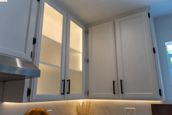 White upper cabinetry with contrasting matte black hardware, under-cabinet lighting, and frosted glass-front cabinets with interior illumination