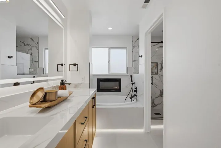 Contemporary bath featuring a dual vanity with wood-finish cabinetry, integrated sinks, and a large mirror with integrated lighting
