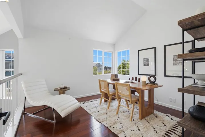 Bright room featuring rich wood-finish flooring, multiple windows providing natural illumination, a vaulted ceiling, and a built-in shelving unit