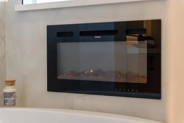 Built-in electric fireplace with a black glass front, integrated into a tiled wall, positioned above a white bathtub surround