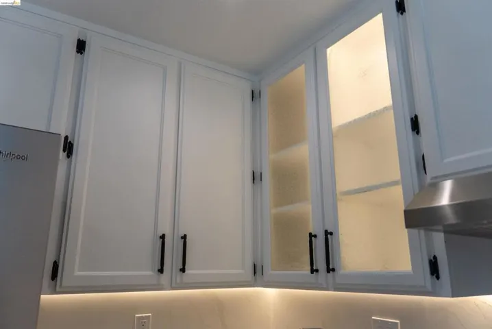 White upper cabinetry featuring black hardware, under-cabinet lighting, and frosted glass cabinet doors with interior illumination