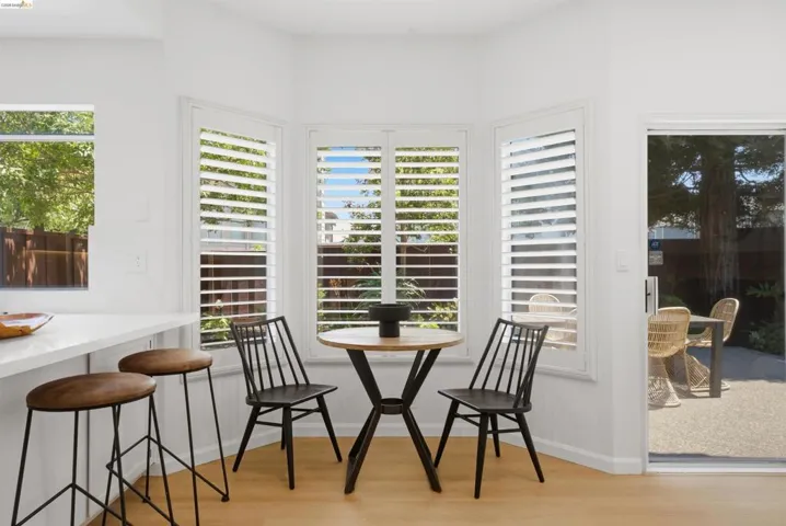 Bright kitchen dining nook featuring a bay window with plantation shutters, wood-finish flooring, and a sliding glass door to the exterior patio