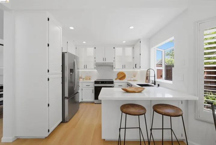 Bright kitchen featuring white cabinetry, stainless steel appliances, a white quartz countertop island with seating, a white subway tile backsplash, and wood-finish flooring