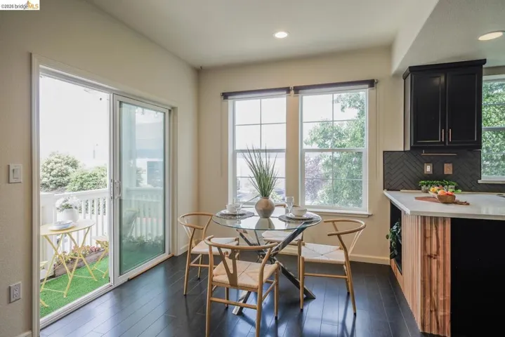 Dining area featuring dark wood-finish flooring, two large windows, a sliding glass door to a balcony, recessed lighting, and a kitchen peninsula with a herringbone tile backsplash and wood paneling
