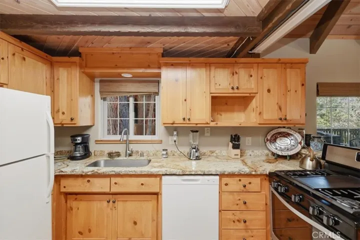 Kitchen sink area with wood cabinets, granite counters, dishwasher, and gas range.