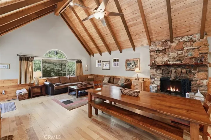 Living and dining area with vaulted wood ceilings, stone fireplace, and large front window.