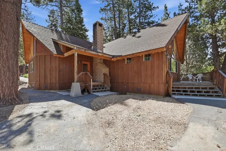 Rear exterior view with wood siding, chimney, and access to the deck area.