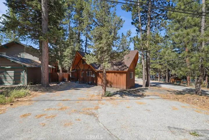 Street-side view of the cabin with paved parking area and tall trees around the property.