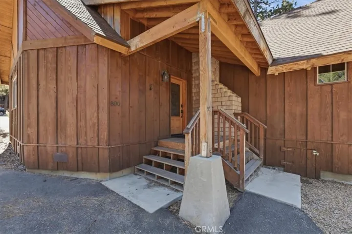 Closer view of the front entry with covered porch, wood siding, and steps to the door.