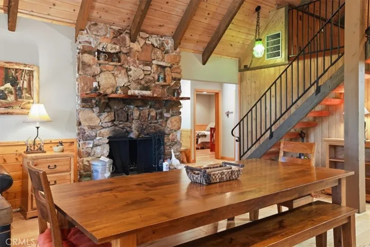 Dining area near the stone fireplace and staircase, with wood floors and cabin-style finishes.