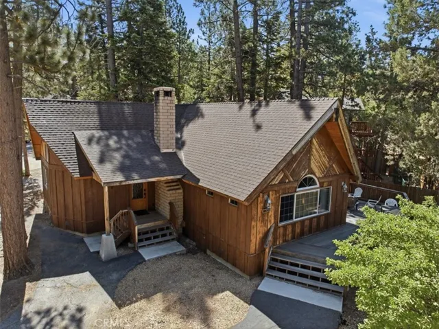 Elevated exterior view showing the cabin, deck, chimney, and mature trees.