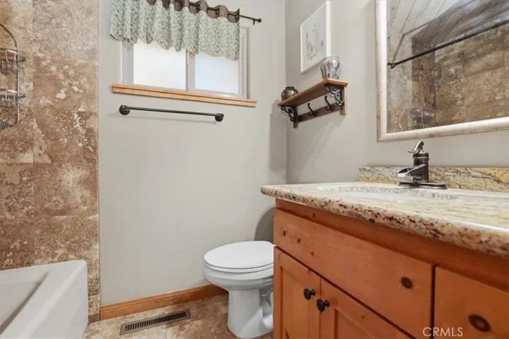 Bathroom with wood vanity, stone-look countertop, tub shower, and neutral finishes.