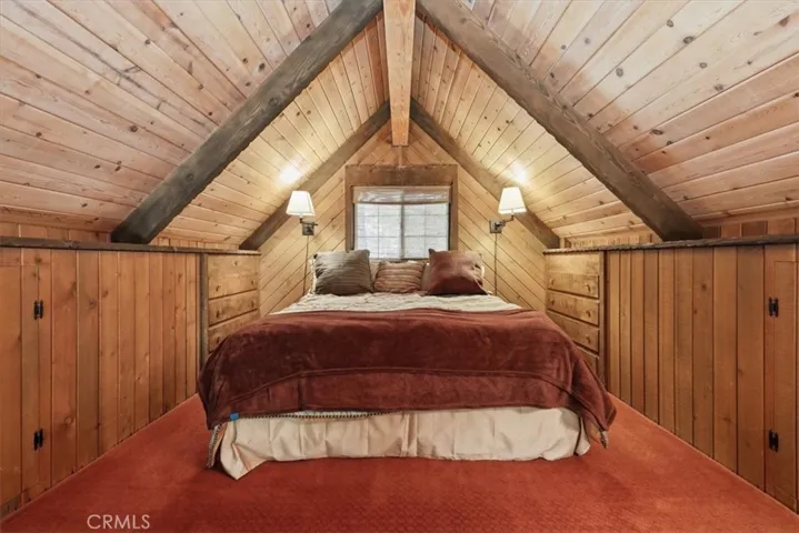 Loft bedroom with wood-paneled ceiling, built-in storage, and warm cabin details.