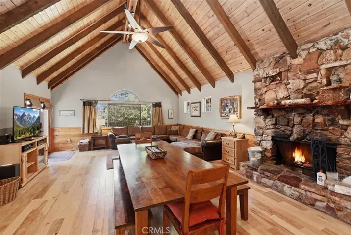 Living and dining area with vaulted wood ceilings, stone fireplace, and large windows.
