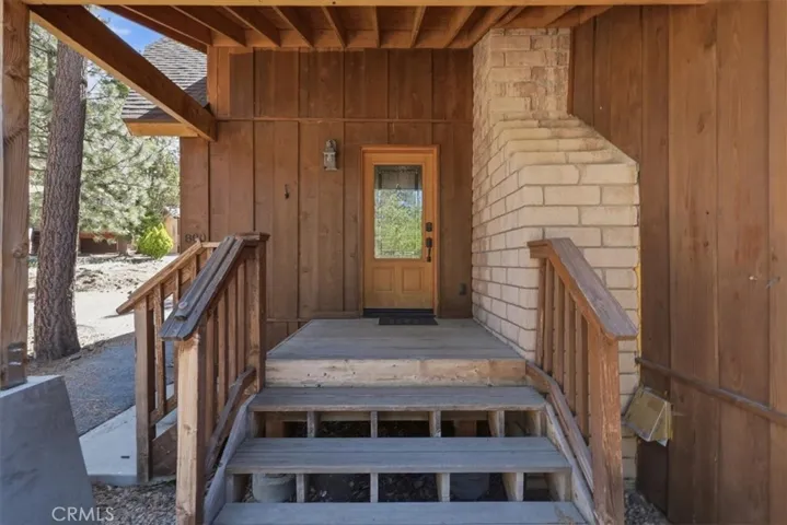 Covered front entry with wood stairs, railing, and stone chimney detail.