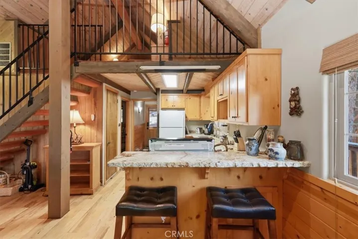 Kitchen view with breakfast bar seating, wood cabinetry, and loft railing above.