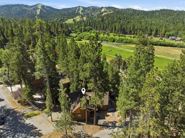 Wide aerial view featuring nearby open land, forested hills, and a distant lake.