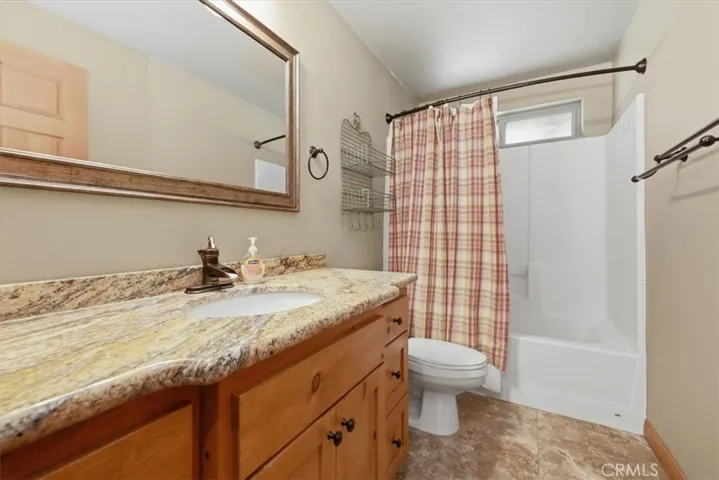Bathroom with wood vanity, granite counter, tub shower, and neutral finishes.