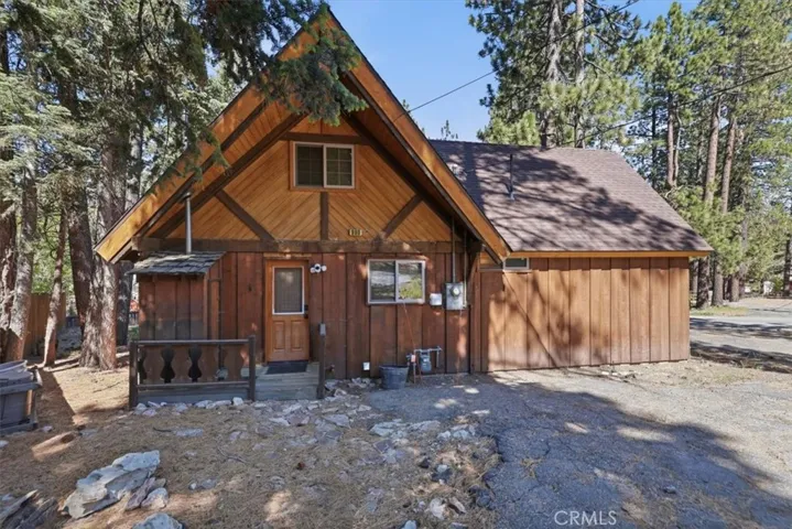 Front exterior view of the cabin with wood siding, steep roofline, and surrounding pine trees.