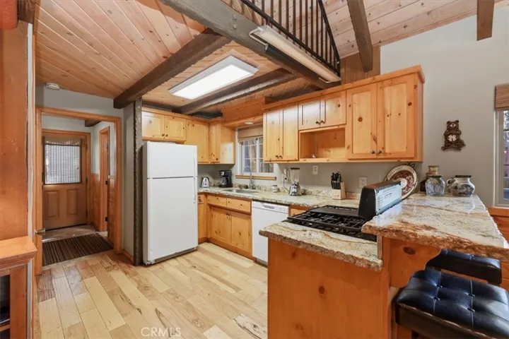 Kitchen with wood cabinetry, granite counters, breakfast bar, and nearby entry hall.