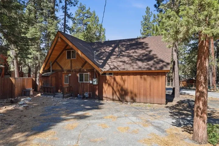 Exterior view of the cabin with wood siding, front entry, and surrounding pine trees.