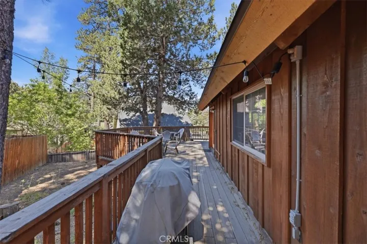 Side deck with wood railing, string lights, and seating area among the trees.
