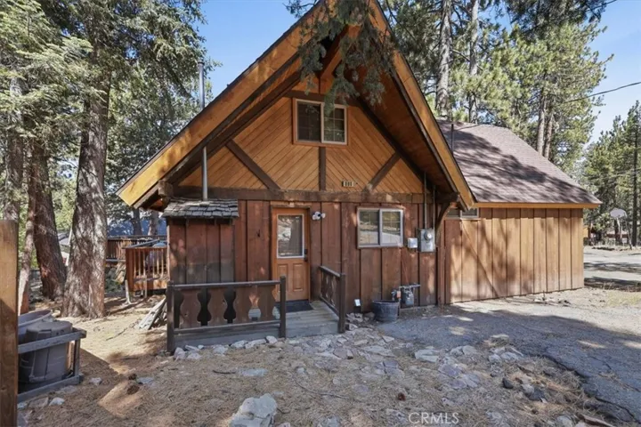 Front exterior view of the cabin with wood siding, steep roofline, and surrounding pine trees.