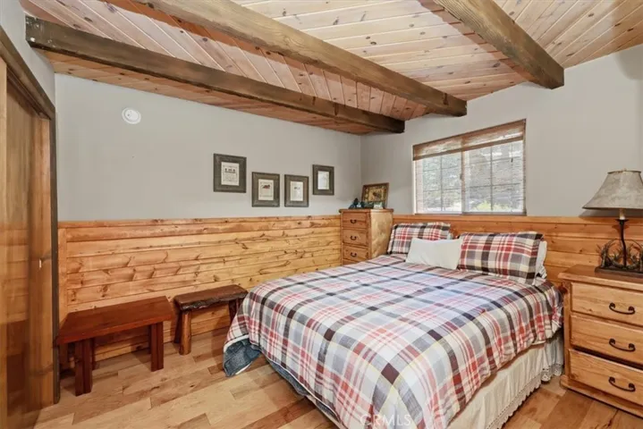 Bedroom with wood accents, exposed ceiling beams, and a window for natural light.