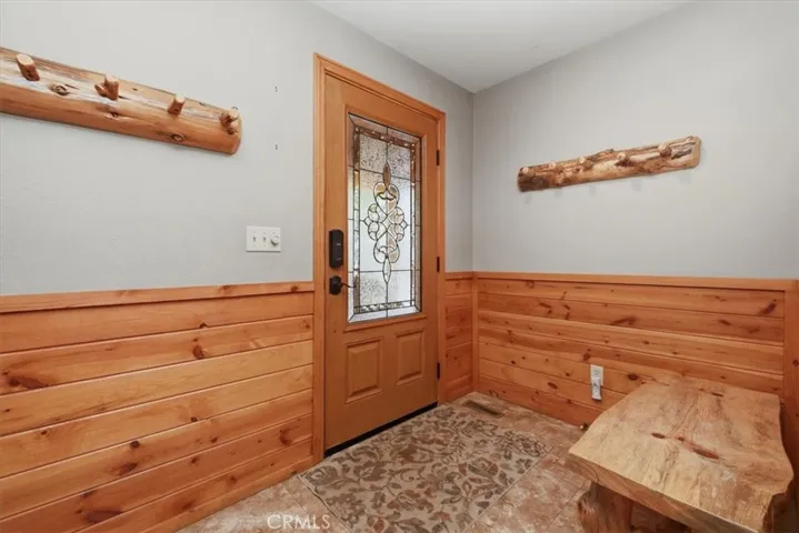 Entry area with decorative front door, wood wainscoting, and built-in wall hooks.
