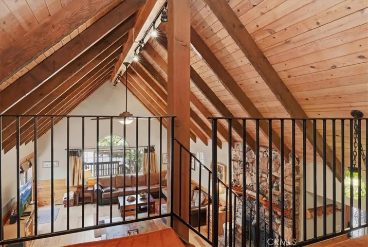 View from the loft overlooking the living room, stone fireplace, and vaulted wood ceiling.