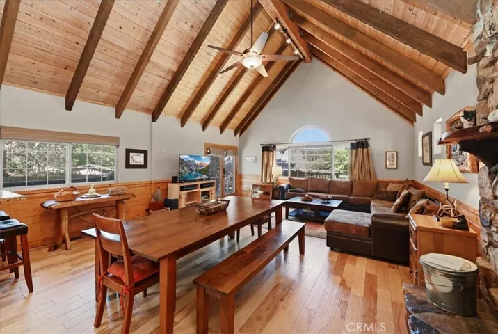 Open living and dining area with vaulted wood-beam ceilings, wood flooring, and a stone fireplace.