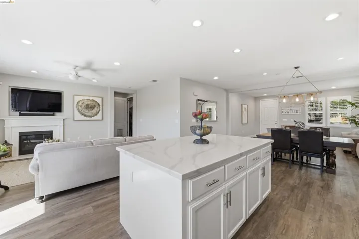 Kitchen featuring white cabinetry, a kitchen island, open floor plan, light stone countertops, and a glass covered fireplace