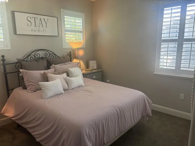 Room featuring two windows with white plantation shutters, neutral wall paint, and dark carpeting