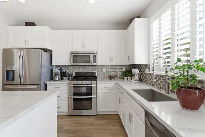 Kitchen with stainless steel appliances, white cabinets, light stone counters, light wood finished floors, and backsplash