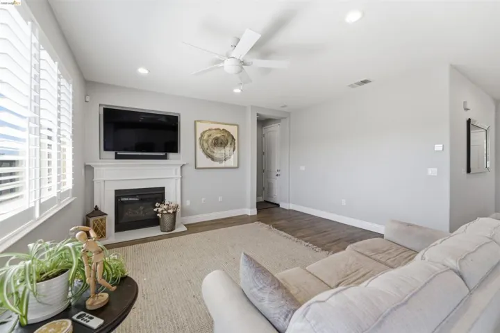 Living area with ceiling fan, a glass covered fireplace, wood finished floors, and recessed lighting