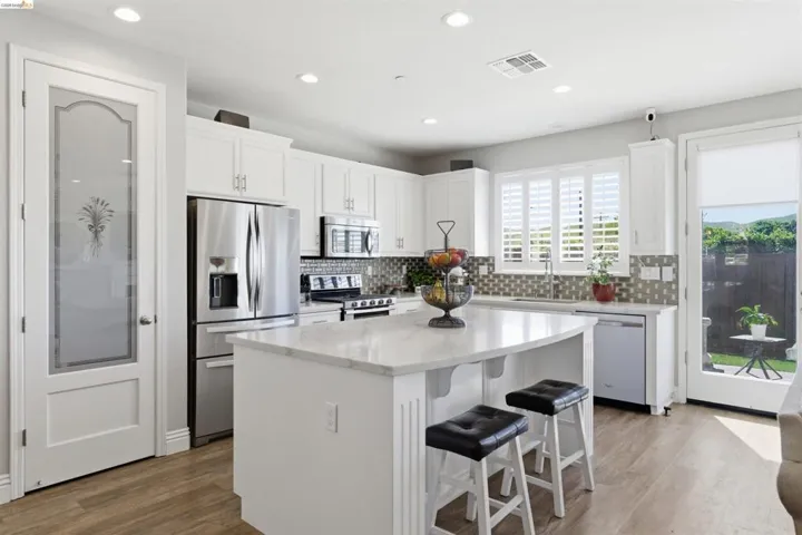 Kitchen with stainless steel appliances, white cabinetry, a kitchen island, a kitchen bar, and light wood-style flooring