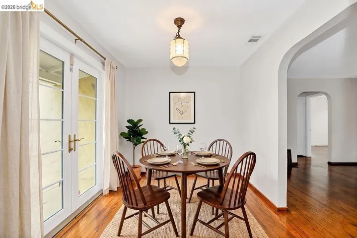 Dining area featuring hardwood flooring, a glass-paned double door, and an arched entryway