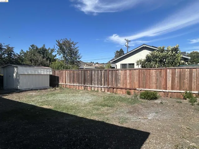 Expansive backyard featuring a wood fence, a detached storage shed, a mixed grass and soil ground cover, and surrounding mature foliage