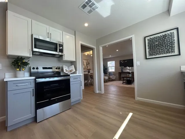 Kitchen featuring two-tone cabinetry with light grey base cabinets and white upper cabinets, stainless steel range, and stainless steel over-the-range microwave
