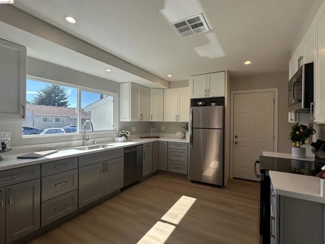 Contemporary kitchen featuring two-tone cabinetry, stainless steel appliances, a large window over the sink, recessed lighting, and wood-finish flooring