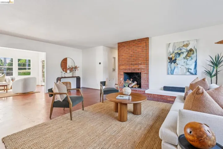 Spacious living area featuring a prominent brick fireplace, white walls, and warm-toned flooring