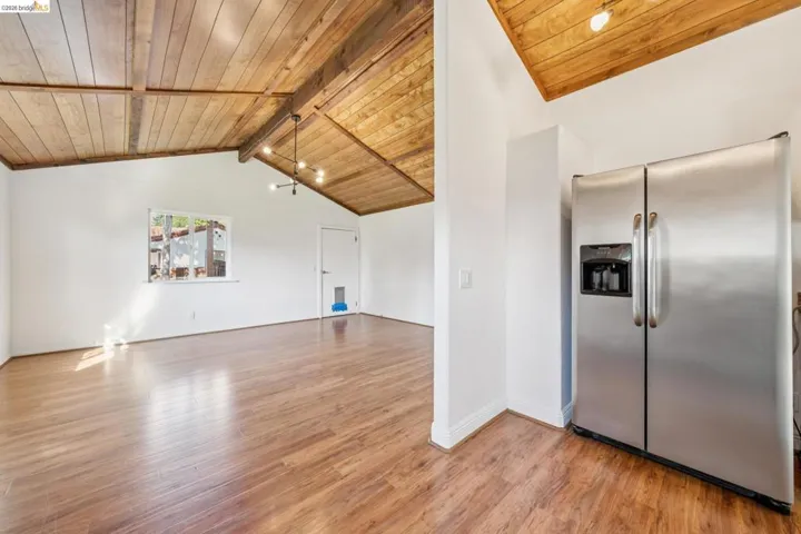 Vaulted wood-plank ceiling with exposed beams, wood-finish flooring, and white walls